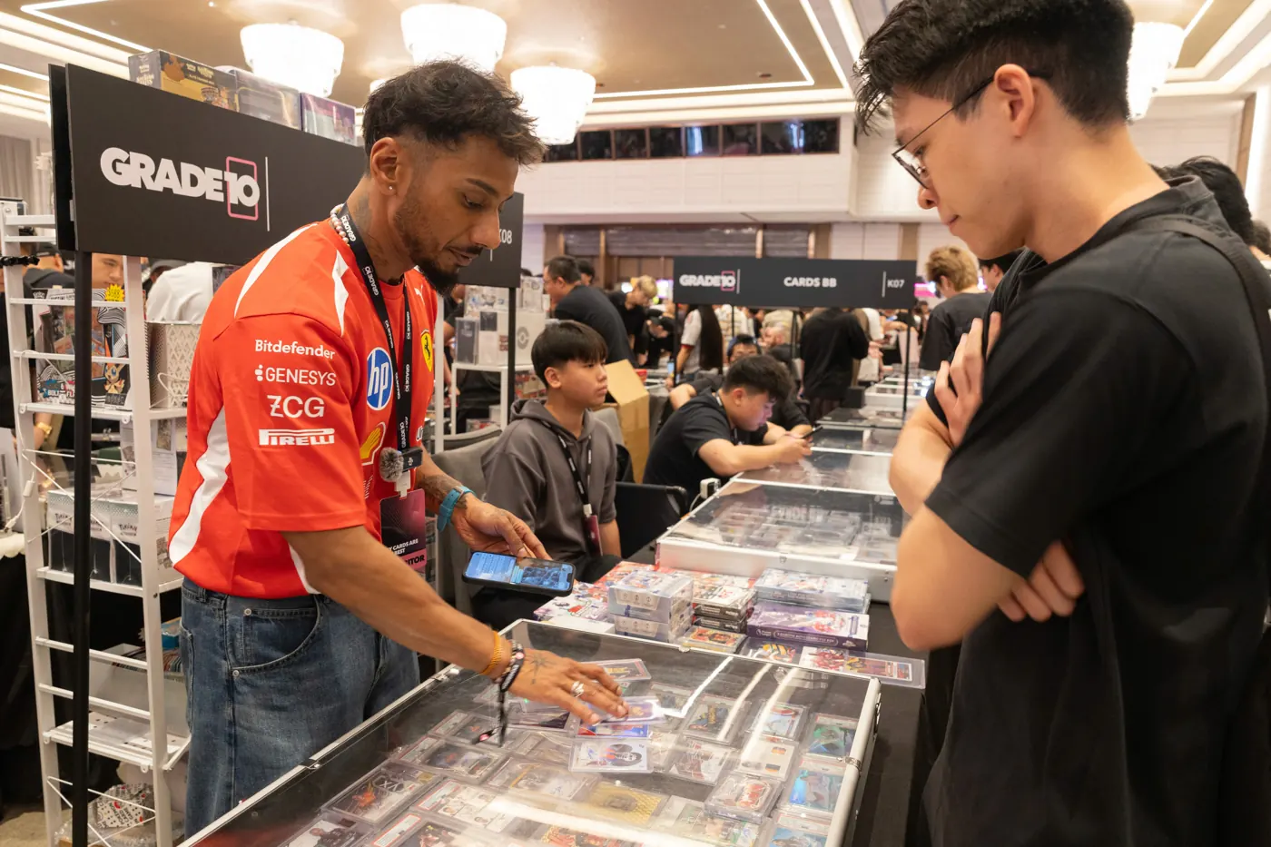 A crowded Grade10 Festival show floor with attendees around trading card tables.